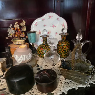 Sale Photo Thumbnail #37: Assortment of vintage collectibles, including a pair of colorful murano-style glass decanters, a small Southwestern pottery vase, a floral porcelain plate, and various decorative trinkets displayed on a lace doily.