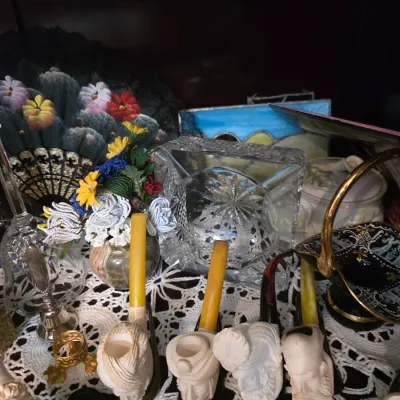 Sale Photo Thumbnail #42: Assortment of vintage collectibles including carved meerschaum pipes, a heavy cut glass ashtray, decorative hand fans, and a black and gold ceramic basket.