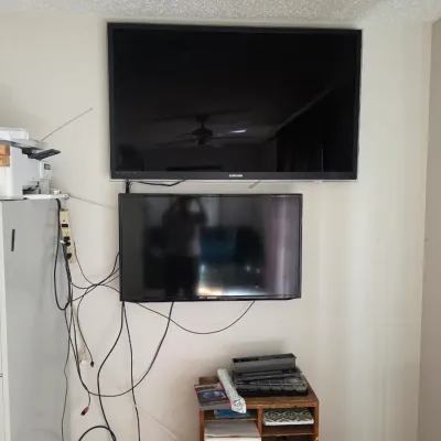 Sale Photo Thumbnail #87: Two wall-mounted Samsung flat-screen televisions, one larger unit positioned above a smaller model, shown with associated wiring.