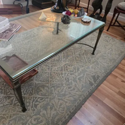 Sale Photo Thumbnail #49: Neoclassical-style metal coffee table with a thick glass top, featuring a lower wooden shelf with pull-out trays, resting on a patterned area rug.