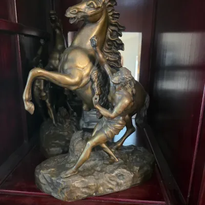 Sale Photo Thumbnail #12: Bronze-finished sculpture depicting a man taming a rearing horse, in the style of the Marly Horses, displayed inside a wooden cabinet.