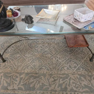 Sale Photo Thumbnail #60: Contemporary glass-top coffee table with a bronze-finished metal frame, featuring a lower shelf holding a wooden tray, displayed on a patterned area rug.
