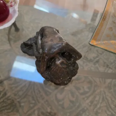 Sale Photo Thumbnail #58: Small bronze or dark-patinated metal sculpture depicting a stylized, abstract human figure, displayed on a glass-top table.