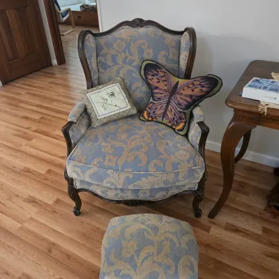 Sale Photo Thumbnail #79: Vintage French Provincial style wingback armchair and matching footstool, upholstered in a blue and gold damask fabric, styled with decorative throw pillows.