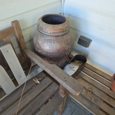 Sale Photo Thumbnail #216: Large antique stoneware crock with a metal band, displayed alongside a wooden bench, metal letters, and terracotta pots.