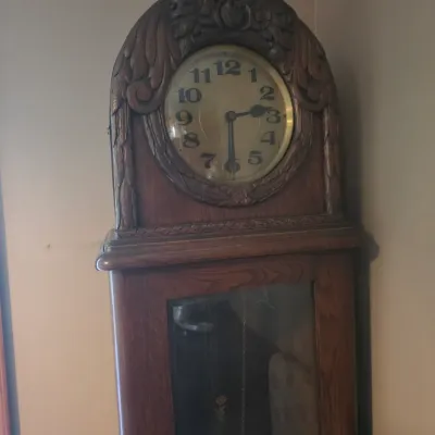 Sale Photo Thumbnail #155: Antique oak grandfather clock featuring an ornately carved bonnet with floral motifs and a glass-fronted pendulum case.