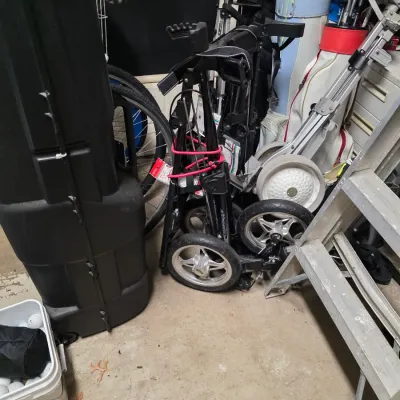 Sale Photo Thumbnail #158: Assorted golf equipment including a hard travel case, multiple golf bags with clubs, and a folded three-wheel push cart.