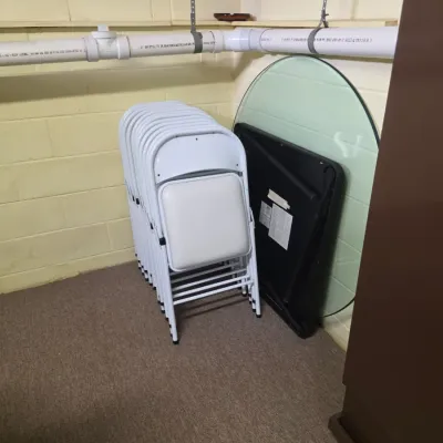 Sale Photo Thumbnail #202: Stack of white metal folding chairs with padded seats, shown alongside a folded black card table and a round glass tabletop.