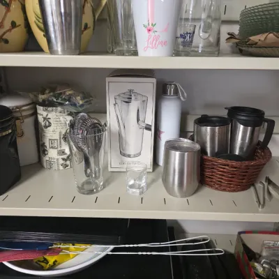 Sale Photo Thumbnail #150: Assorted kitchenware and drinkware on metal shelving, including travel mugs, a boxed coffee carafe, canisters, and bar tools.