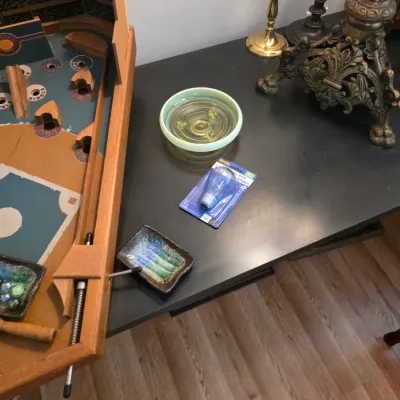 Sale Photo Thumbnail #64: Assorted tabletop items including a small green glass dish, a packaged light bulb, a small glazed ceramic tray, and an ornate brass lamp base.