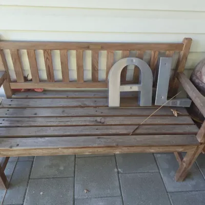 Sale Photo Thumbnail #214: Weathered wooden garden bench with slatted seat and backrest, holding two large metal letters.