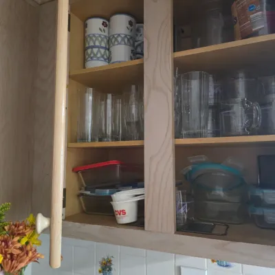 Sale Photo Thumbnail #131: Assorted kitchen glassware, mugs, and food storage containers organized inside a light wood cabinet.