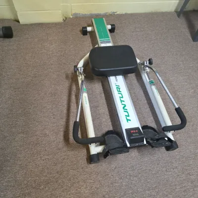 Sale Photo Thumbnail #199: Vintage Tunturi folding rowing machine with hydraulic resistance cylinders, white frame, and black padded seat.
