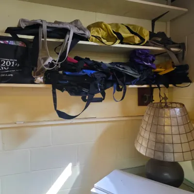Sale Photo Thumbnail #188: Assorted tote bags, duffels, and backpacks stored on wooden shelves, alongside a table lamp featuring a capiz shell shade.