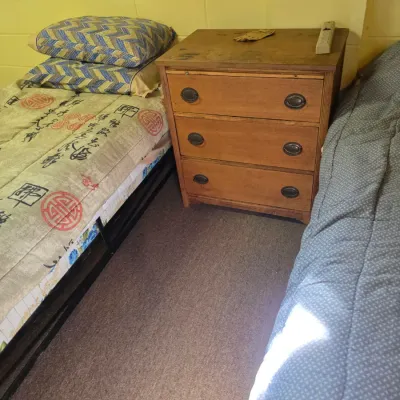 Sale Photo Thumbnail #184: Vintage three-drawer wooden nightstand with oval metal pulls, positioned between two twin beds.