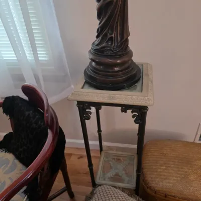 Sale Photo Thumbnail #53: Neoclassical-style metal pedestal stand with a square stone-inlaid top and a lower shelf, supporting a bronze-finished statue base.