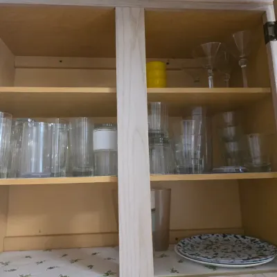 Sale Photo Thumbnail #132: Assorted glassware, including tumblers and stemmed cocktail glasses, arranged on shelves inside a light wood cabinet.