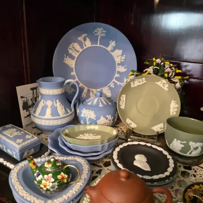 Sale Photo Thumbnail #35: Collection of vintage Wedgwood jasperware in blue, green, and black, featuring classical relief designs on plates, a pitcher, a lidded sugar bowl, and a teacup.