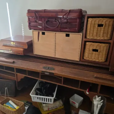 Sale Photo Thumbnail #106: Vintage oak roll-top desk with built-in cubbies, topped with various storage boxes, including a woven wicker suitcase and small wooden drawers.