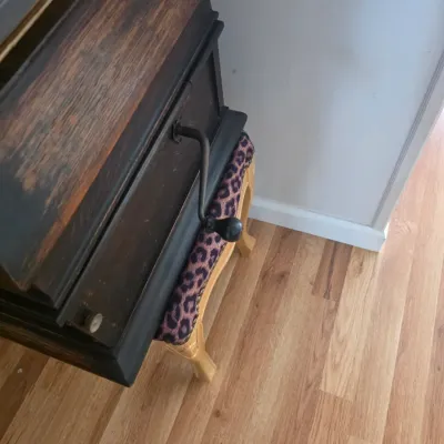 Sale Photo Thumbnail #75: Vintage hand-crank phonograph cabinet in dark wood, positioned next to a small footstool with leopard print upholstery.