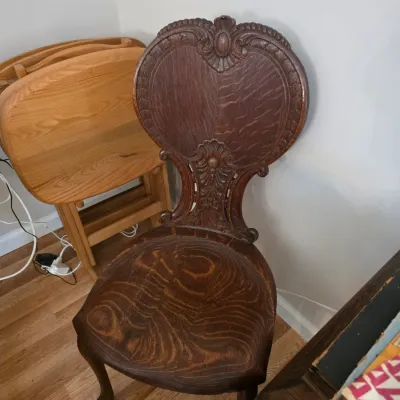 Sale Photo Thumbnail #76: Antique carved oak side chair featuring a balloon back with ornate scrollwork and a contoured wooden seat showing prominent grain.