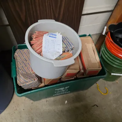 Sale Photo Thumbnail #160: Assorted rolls of coins, including pennies, nickels, and dimes, stored in a plastic bucket and cardboard boxes within a green recycling bin.