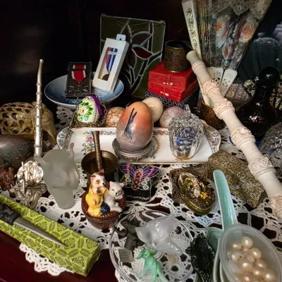 Sale Photo Thumbnail #41: Eclectic collection of vintage collectibles and trinkets, including decorative eggs, small figurines, a carved pipe, and various ornamental boxes displayed on a lace doily.