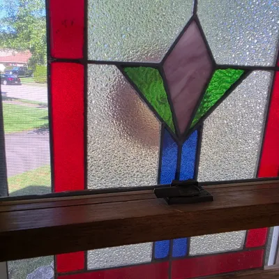 Sale Photo Thumbnail #142: Vintage stained glass window panel featuring a geometric floral design with red, green, purple, and blue accents set in textured clear glass.