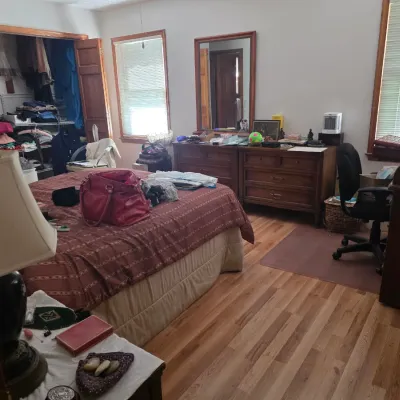 Sale Photo Thumbnail #102: Bedroom furniture set including a wooden double dresser with matching mirror, a wooden desk, and an office chair, alongside a bed with patterned bedding.