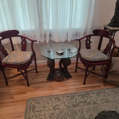 Sale Photo Thumbnail #55: Pair of Asian-style carved mahogany horseshoe-back armchairs with patterned seat cushions, flanking an octagonal glass-top side table with a carved pedestal base.