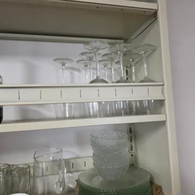 Sale Photo Thumbnail #148: Assorted glassware including stemmed wine glasses stored upside down, clear glass mugs, a pitcher, and a stack of small bowls on a metal shelving unit.