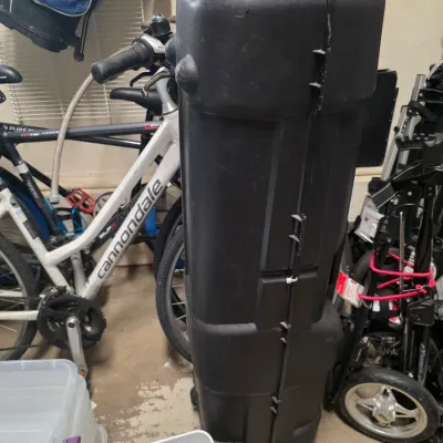 Sale Photo Thumbnail #159: Large black molded plastic hard-shell travel case, suitable for golf clubs or other sports equipment, shown standing upright in a garage.