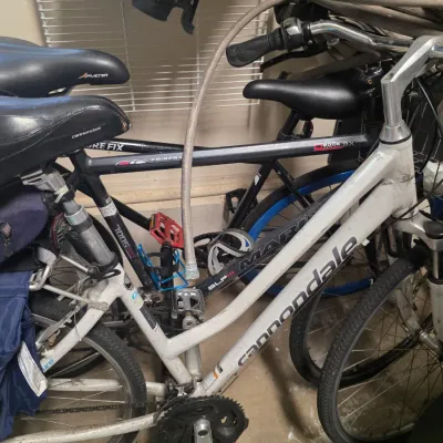 Sale Photo Thumbnail #163: A group of bicycles including a white Cannondale step-through frame hybrid bike and a black Marin Fairfax hybrid bike, showing signs of use.