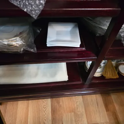 Sale Photo Thumbnail #27: Assorted tableware, including a stack of white square plates and wrapped porcelain dishes, stored on dark wood shelves.
