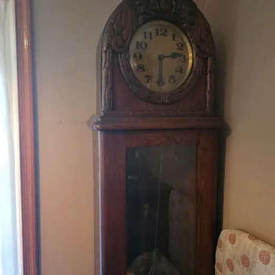 Sale Photo Thumbnail #154: Antique oak grandfather clock featuring an ornate carved bonnet with floral motifs and a glass-fronted pendulum case.