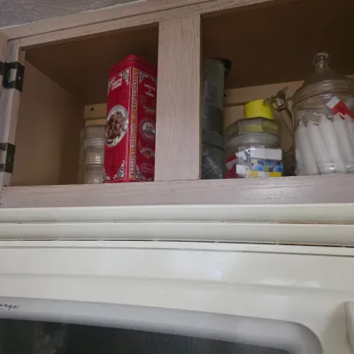 Sale Photo Thumbnail #128: Assorted kitchen storage items including a vintage red Amaretti di Saronno tin, glass jars, and candles, displayed in an open wooden cabinet above an Amana Radarange microwave.