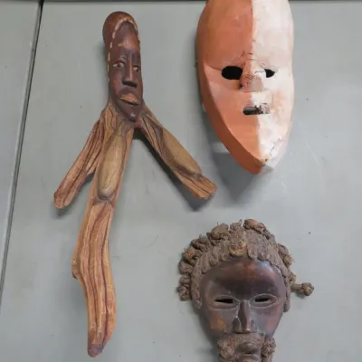Sale Photo Thumbnail #27: Three hand-carved African-style wooden masks and figures, including a two-toned mask, a mask with textured hair detailing, and a stylized elongated figure.