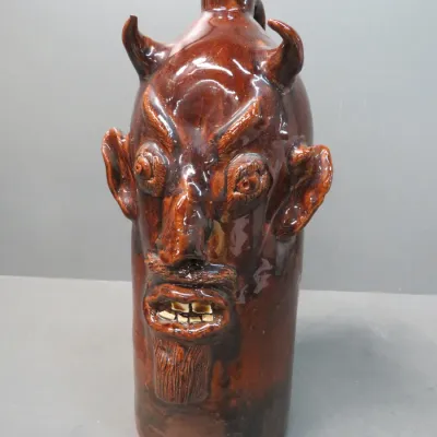 Sale Photo Thumbnail #3: Southern folk art devil face jug with a brown glaze, featuring prominent horns, ears, a goatee, and bared teeth.
