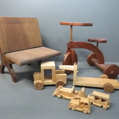 Sale Photo Thumbnail #22: Collection of vintage wooden toys and children's furniture, including a miniature school desk, a wooden tricycle, and various toy trucks and cars.