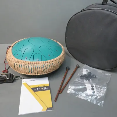 Sale Photo Thumbnail #14: Hopwell steel tongue drum in teal with a woven rope border, accompanied by two mallets, a music book, accessories, and a black zippered carrying case.