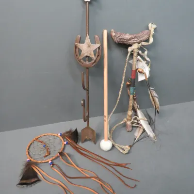 Sale Photo Thumbnail #12: Collection of Western and Native American style decor, including a metal arrow wall hook with a horseshoe and star, a dreamcatcher, a decorative staff with feathers, and a mallet.