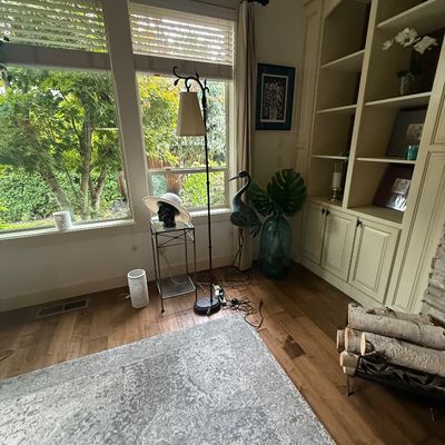 Eclectic living room corner featuring a wrought iron floor lamp, a metal heron sculpture, a large blue glass floor vase, and a modern...