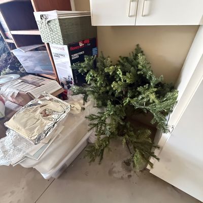 Artificial Christmas tree branches stored in a garage alongside various storage bins, boxes, and household items.