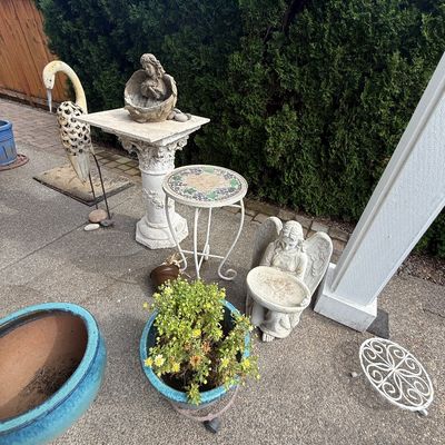 Assorted garden decor including concrete angel statues, a pedestal, a mosaic-top side table, a metal crane sculpture, and blue glazed...