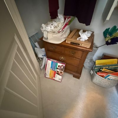 Traditional three-drawer wooden nightstand or end table with brass hardware, shown in a closet with various storage baskets and books.