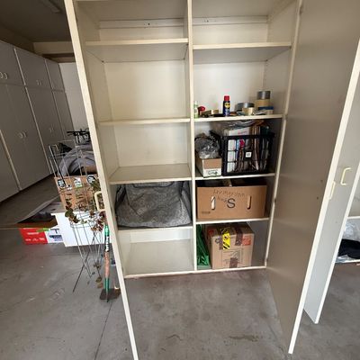 Large white laminate storage cabinet with double doors, adjustable shelving, and various storage boxes inside.