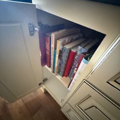 Collection of assorted cookbooks, including "The Moosewood Cookbook" by Mollie Katzen, stored inside a cream-colored kitchen...