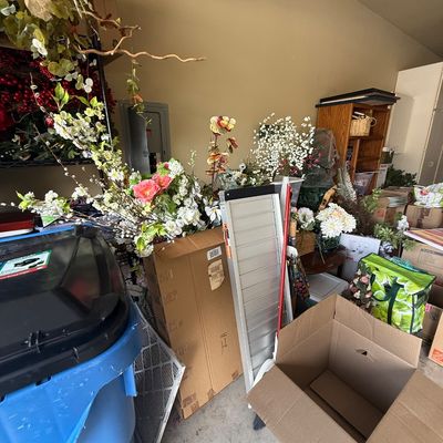 Assorted garage items including artificial floral arrangements, a folding aluminum ramp, cardboard boxes, and a blue recycling bin.