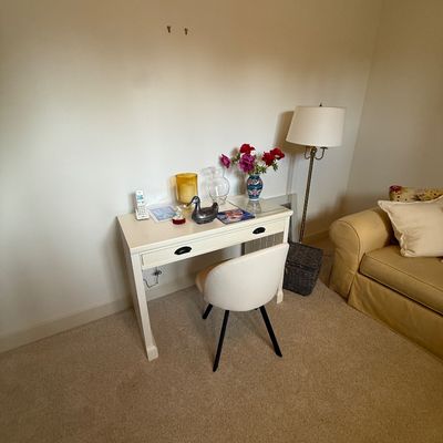 White wooden writing desk with a single drawer, paired with a modern white upholstered chair featuring black legs.