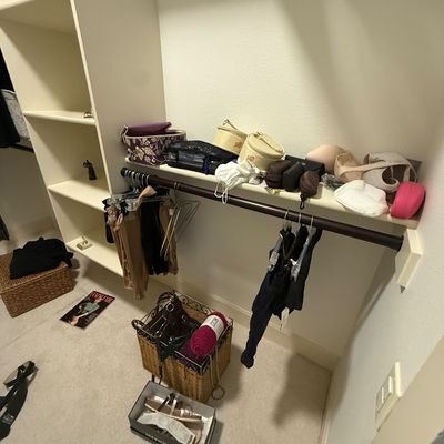 Assorted closet items including handbags, cosmetic cases, clothing on hangers, and a wicker basket with yarn, displayed on shelves and a...
